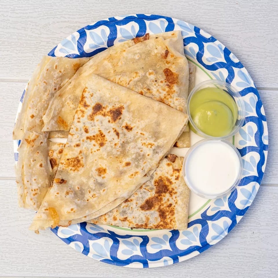 Golden-brown quesadillas on a blue and white paper plate with green and white dipping sauces.