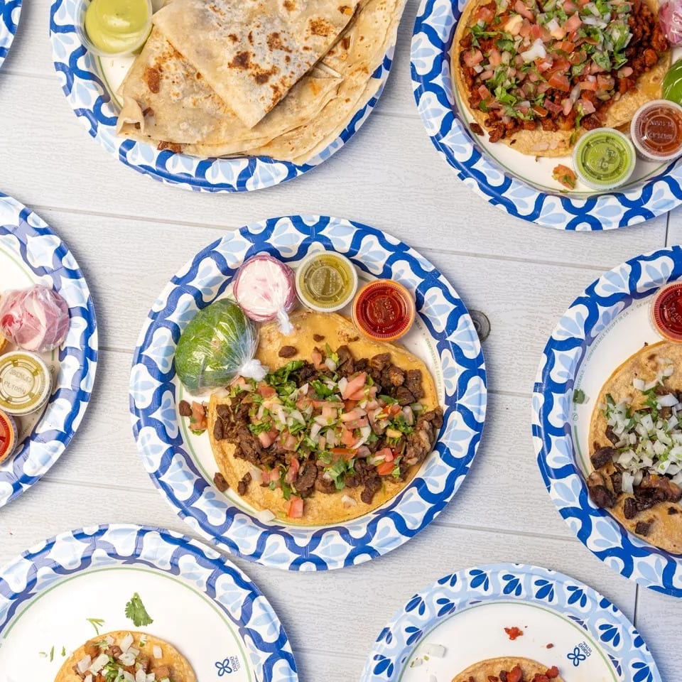Overhead view of multiple plates of tacos and quesadillas on blue and white paper plates.