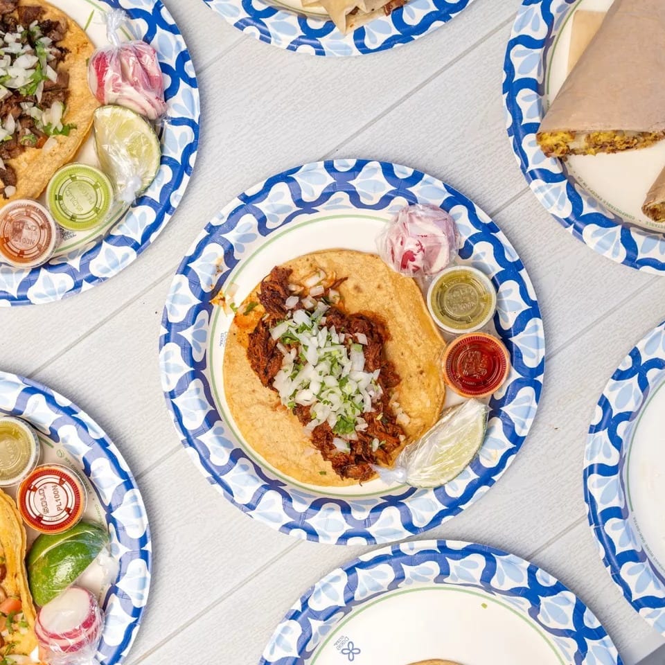 Overhead view of several tacos and burritos on blue and white paper plates with various salsas and limes.