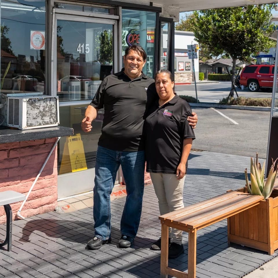 Two restaurant owners, a man and a woman, stand proudly outside their establishment.
