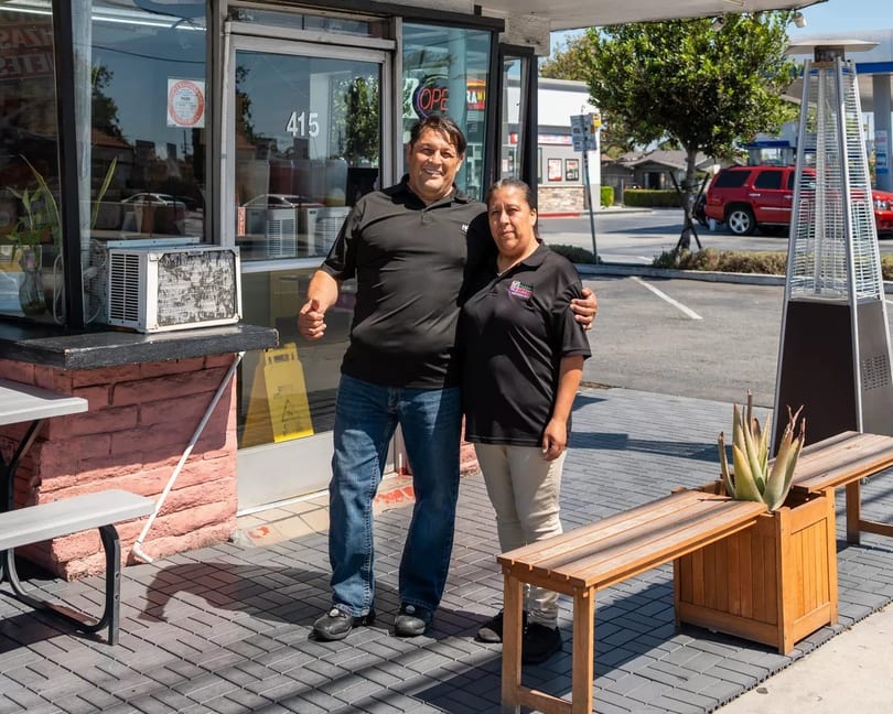Two restaurant owners, a man and a woman, stand proudly outside their establishment.