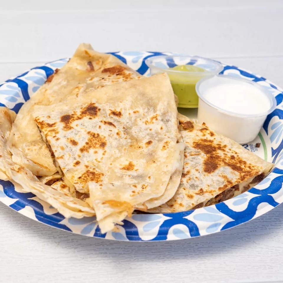 Quesadillas on a blue and white paper plate with sides of guacamole and sour cream.