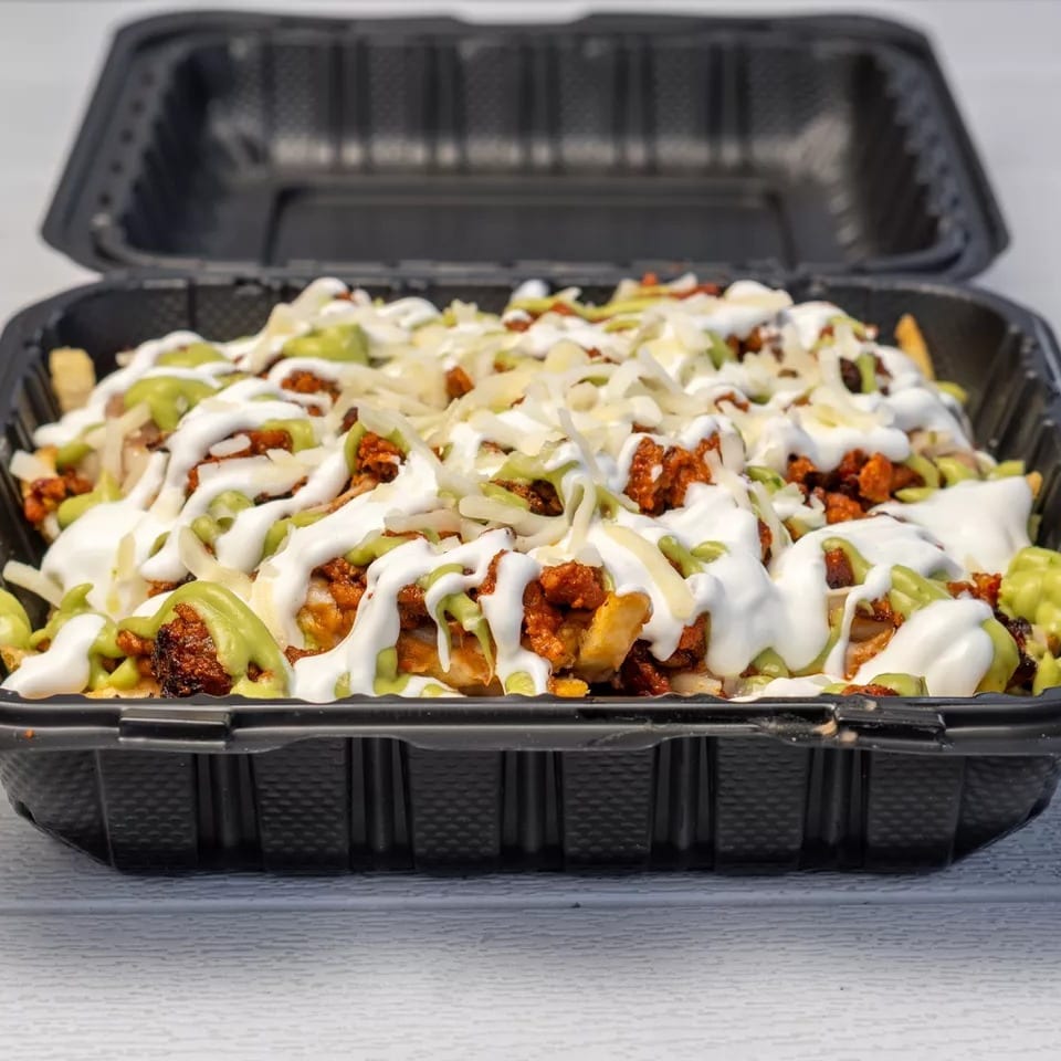Loaded fries with chorizo, shredded cheese, sour cream, and guacamole in a black takeout container.